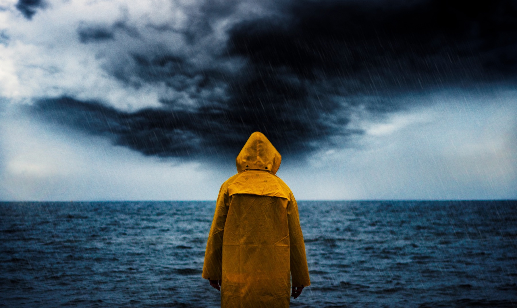 Person in a yellow raincoat standing calmly facing a stormy sea